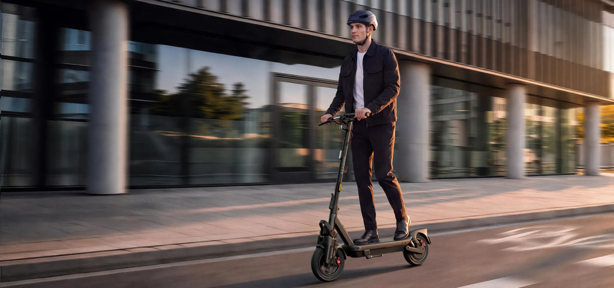 Conducteur casqué roulant sur la Ninebot MAX G3 Pro E dans une rue bordée d'immeubles